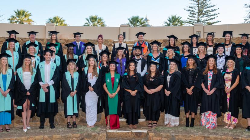 Group photo of Geraldton Universities Centre 2024 graduates. The group are all wearing their respective gowns that correlate with their degree, and they are all posing professionally and smiling at the camera.
